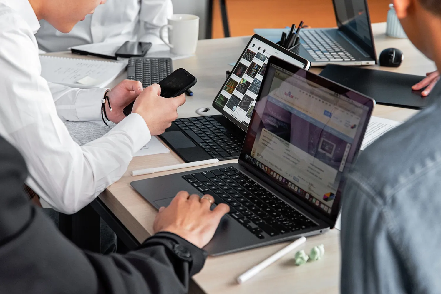 Çalışanlar, modern bir ofiste laptop ve akıllı telefonlar kullanarak iş tartışması yapıyor.